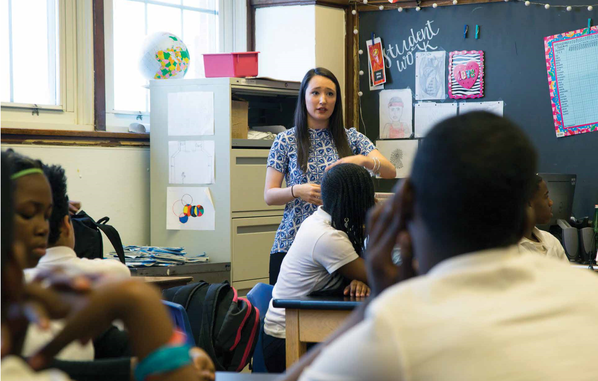 Teacher teaching students in a classroom with a blackboard and pictures behind her